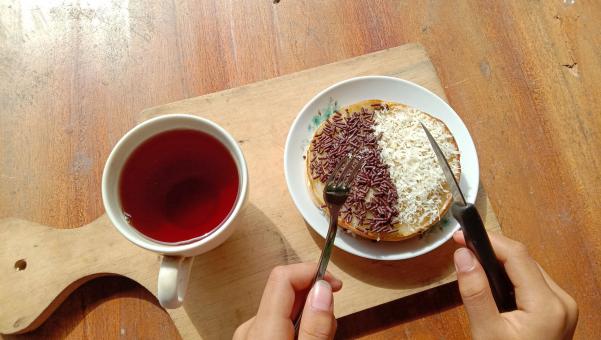 A photo of someone eating a mini martabak and drinking a cup of 