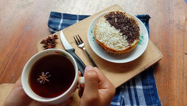 A photo of someone eating a mini martabak and drinking a cup of 