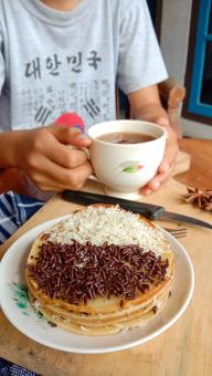 A photo of someone eating a mini martabak and drinking a cup of 