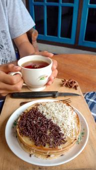 A photo of someone eating a mini martabak and drinking a cup of 